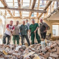 Sechs Arbeiter stehen auf einem Schuttberg im Gebäude während der Sanierungsarbeiten